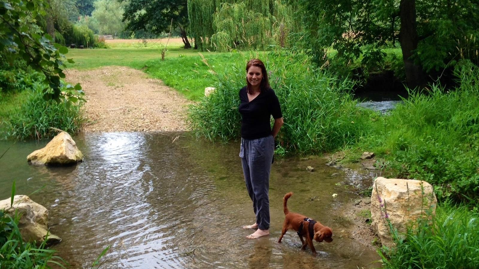 a woman standing in a stream with a dog