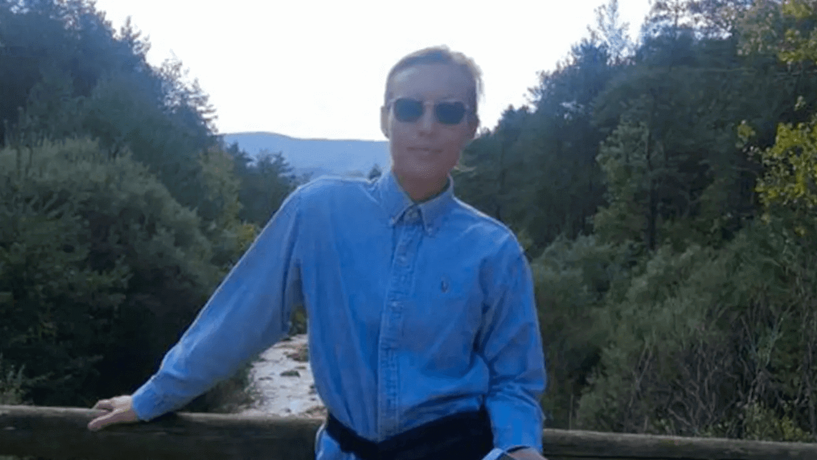 a man wearing sunglasses and standing on a bridge