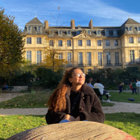 a woman sitting in a park with a large building in the background with Musée Rodin in the background