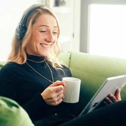 a woman sitting on a couch holding a cup and a tablet