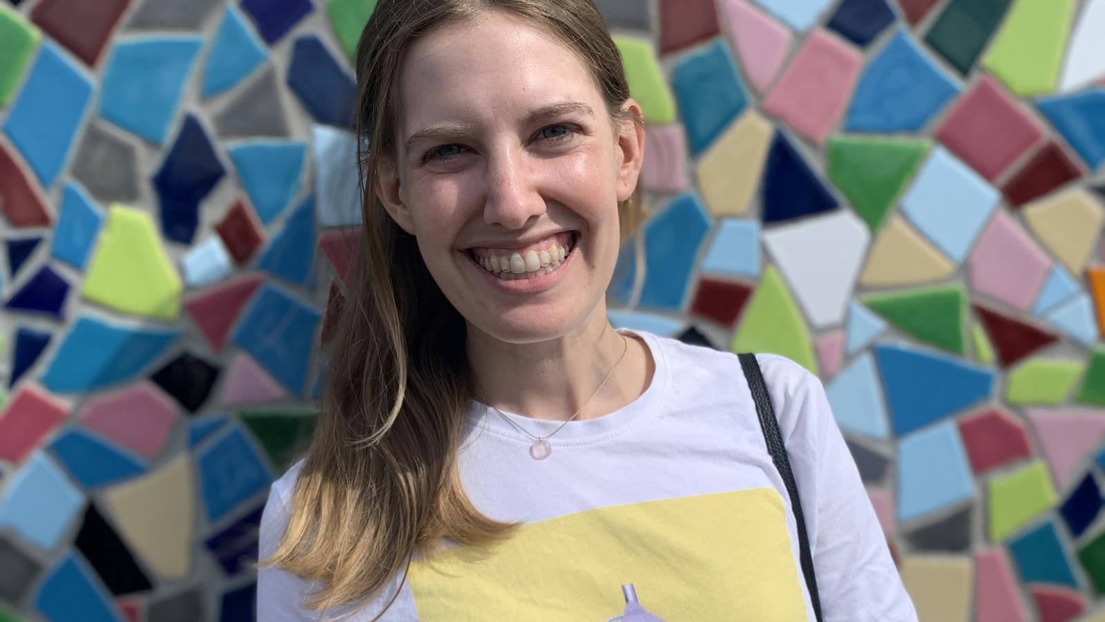 a woman smiling in front of a colorful mosaic wall