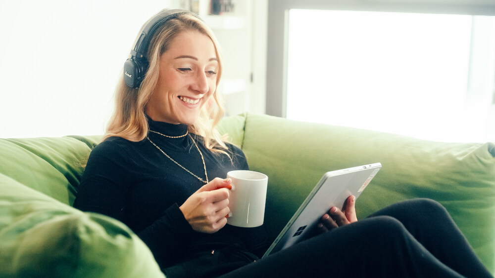 a woman sitting on a couch holding a cup and a tablet