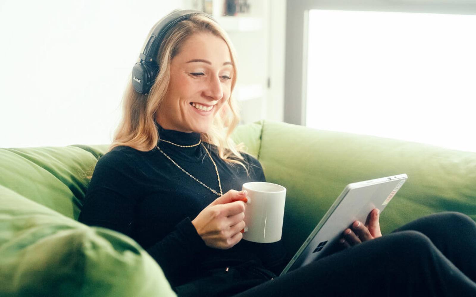 a woman sitting on a couch holding a cup and a tablet