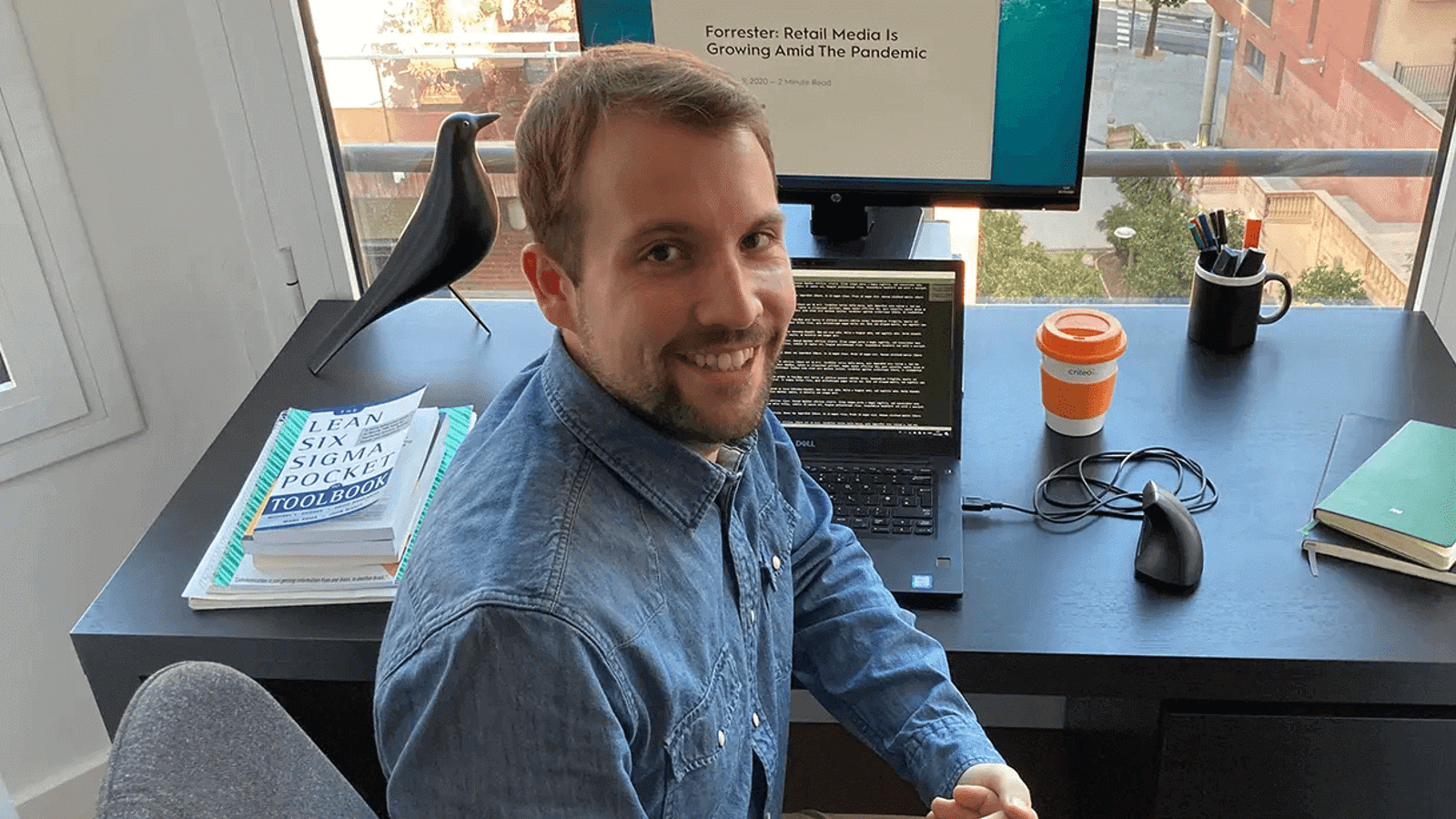 a man sitting at a desk with a computer and a bird on the window