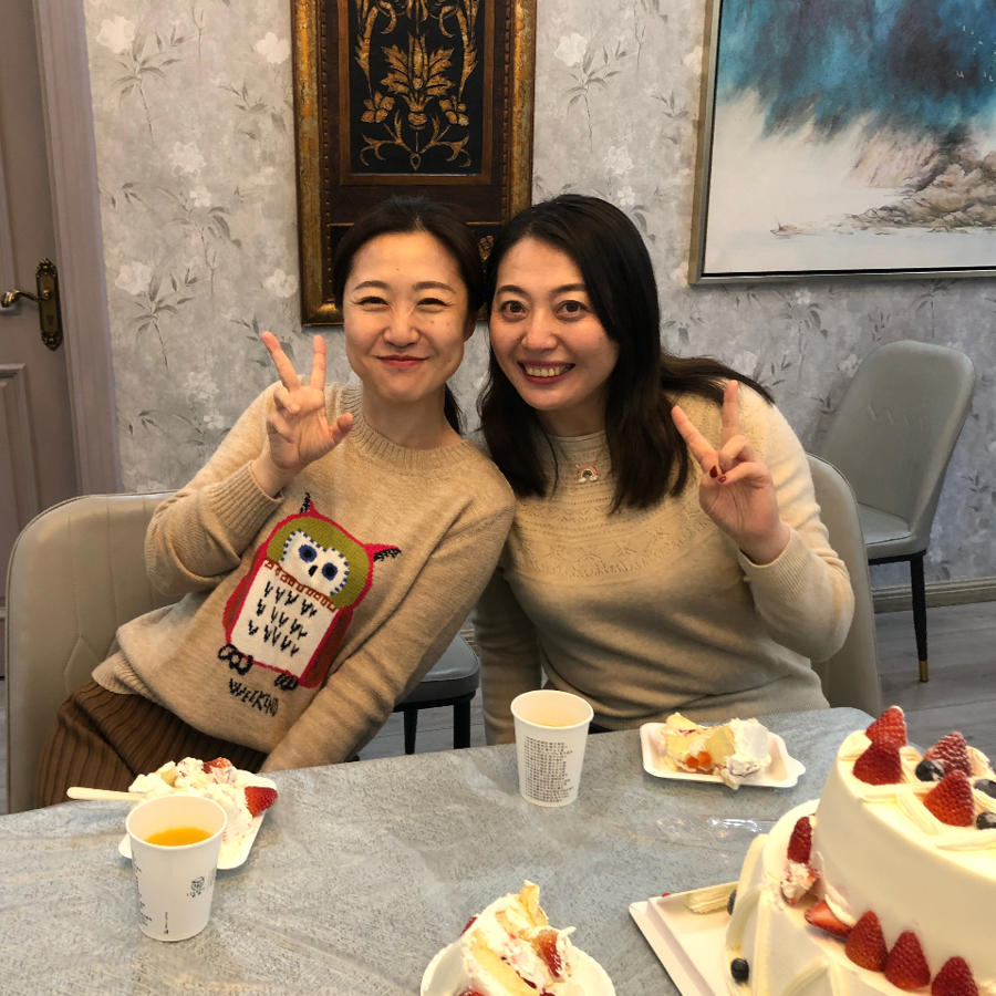 two women sitting at a table with a cake