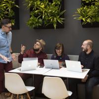 a group of people sitting around a table with laptops